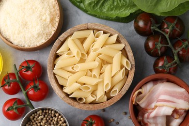 Photo of Raw pasta, bacon and fresh ingredients on light grey table, flat lay