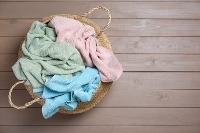 Photo of Wicker laundry basket with towels on wooden background, top view. Space for text