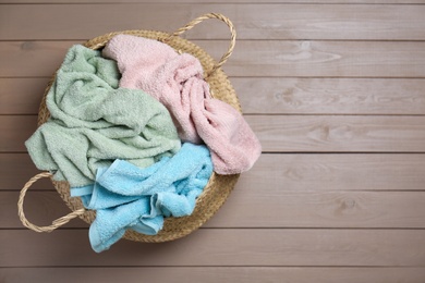 Wicker laundry basket with towels on wooden background, top view. Space for text