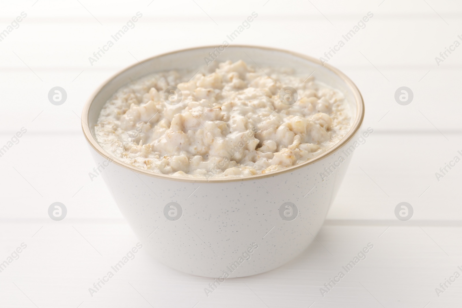 Photo of Tasty boiled oatmeal in bowl on white table, closeup