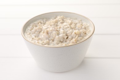 Tasty boiled oatmeal in bowl on white table, closeup