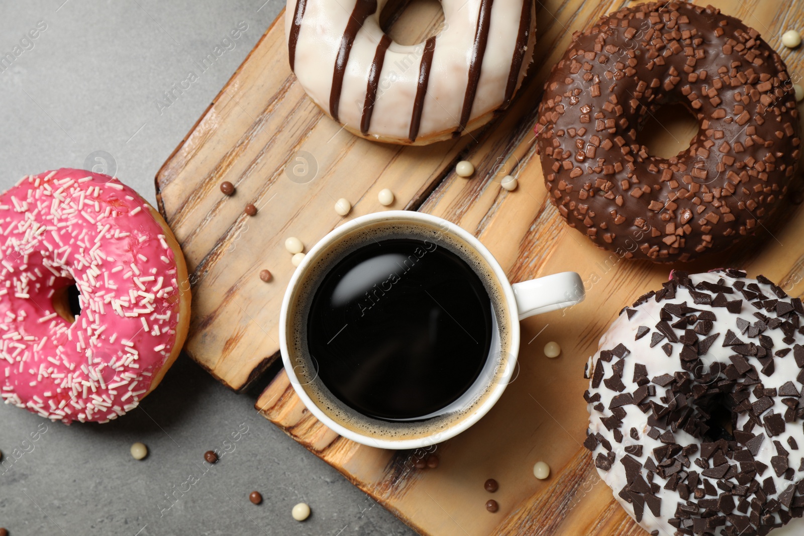 Photo of Yummy donuts with sprinkles and coffee on grey table, flat lay