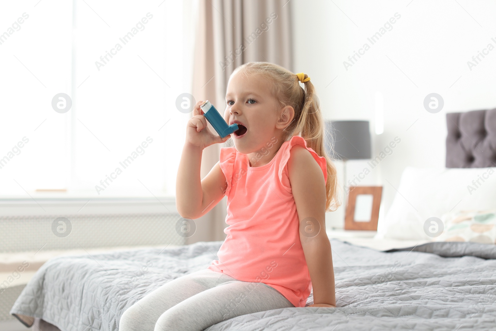 Photo of Little girl using asthma inhaler in bedroom