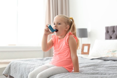 Photo of Little girl using asthma inhaler in bedroom