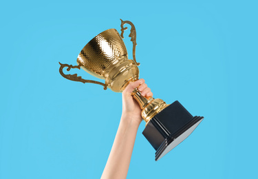 Photo of Woman holding gold trophy cup on light blue background, closeup