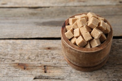 Photo of Bowl with brown sugar cubes on wooden table, closeup. Space for text