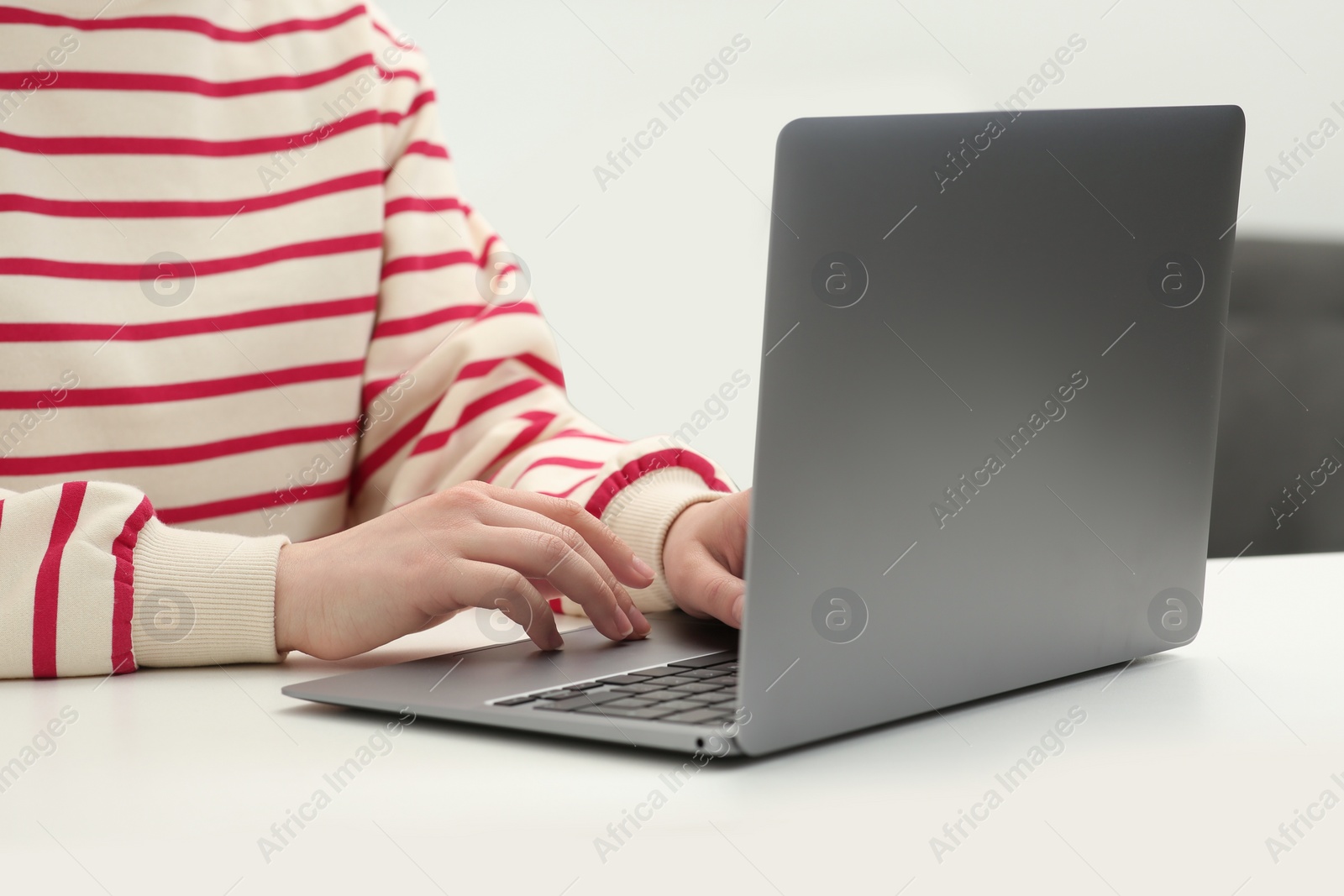 Photo of Woman using laptop at white table indoors, closeup