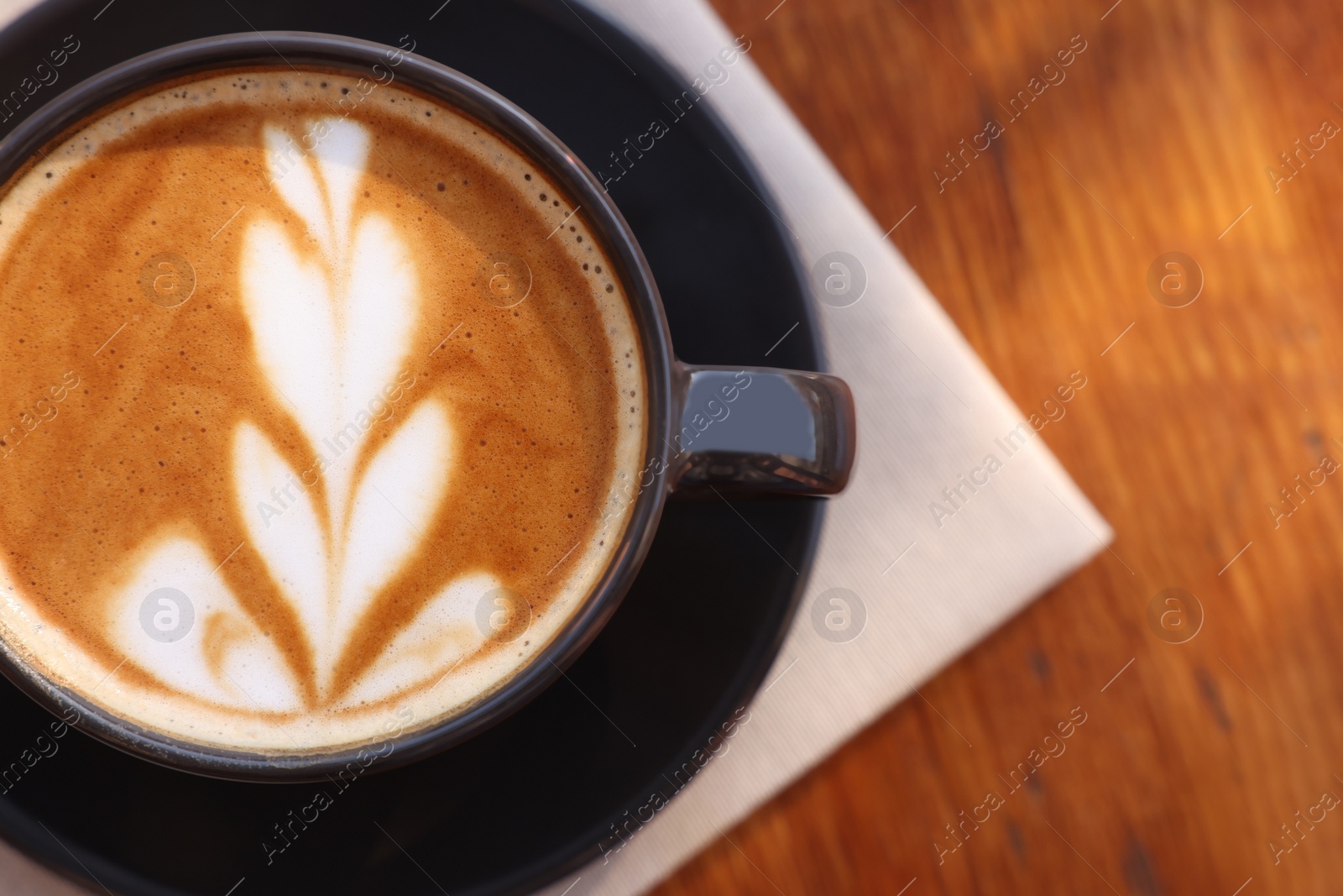 Photo of Cup of aromatic coffee with foam on wooden table, top view. Space for text