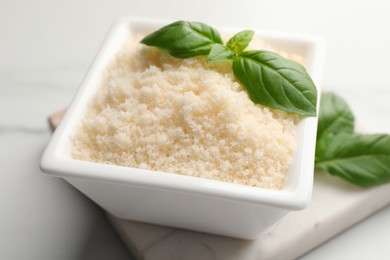 Photo of Square bowl with grated parmesan cheese and basil on white table, closeup
