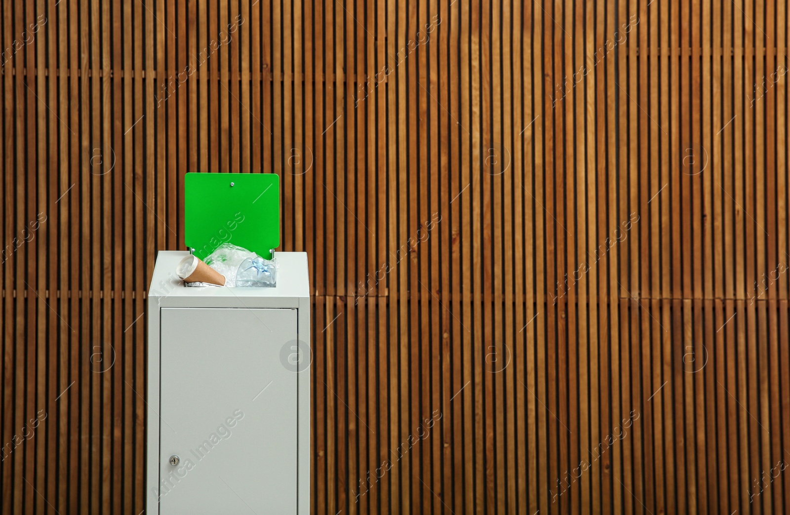 Photo of Overfilled trash bin near wooden wall, space for text. Recycling concept