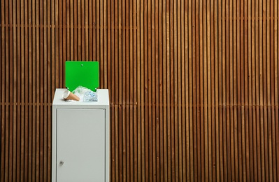 Overfilled trash bin near wooden wall, space for text. Recycling concept