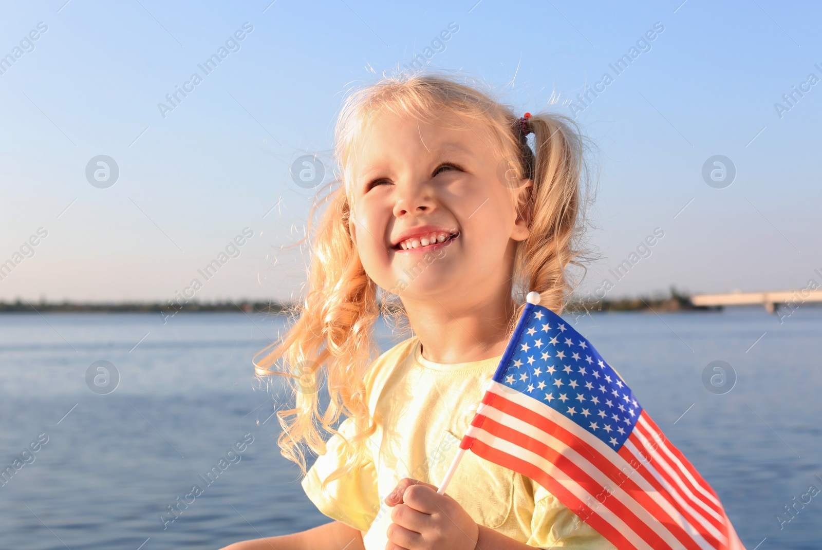 Photo of Cute little girl with American flag near river on sunny day