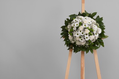 Photo of Funeral wreath of flowers on wooden stand against grey background. Space for text