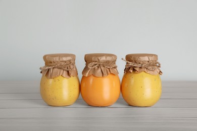 Jars with preserved fruit jams on white wooden table