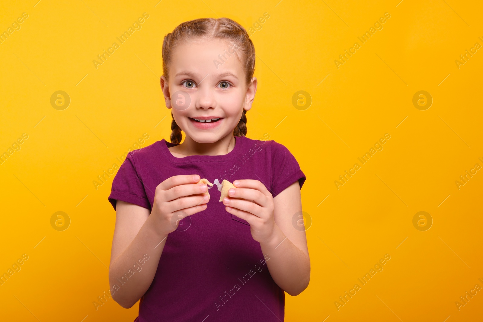 Photo of Cute girl holding tasty fortune cookie with prediction on orange background