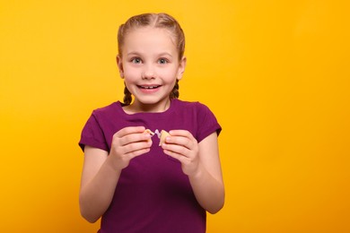 Cute girl holding tasty fortune cookie with prediction on orange background