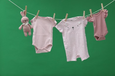 Different baby clothes and bunny toy drying on laundry line against green background