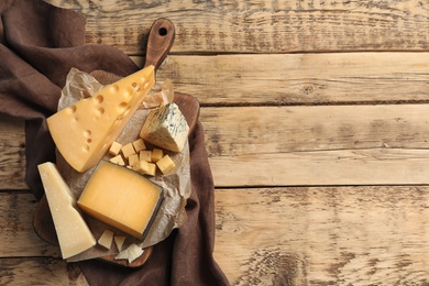 Photo of Different delicious cheeses served on wooden table, top view. Space for text