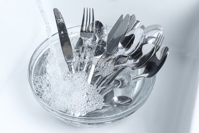 Photo of Washing silver spoons, forks and knives under stream of water in kitchen sink