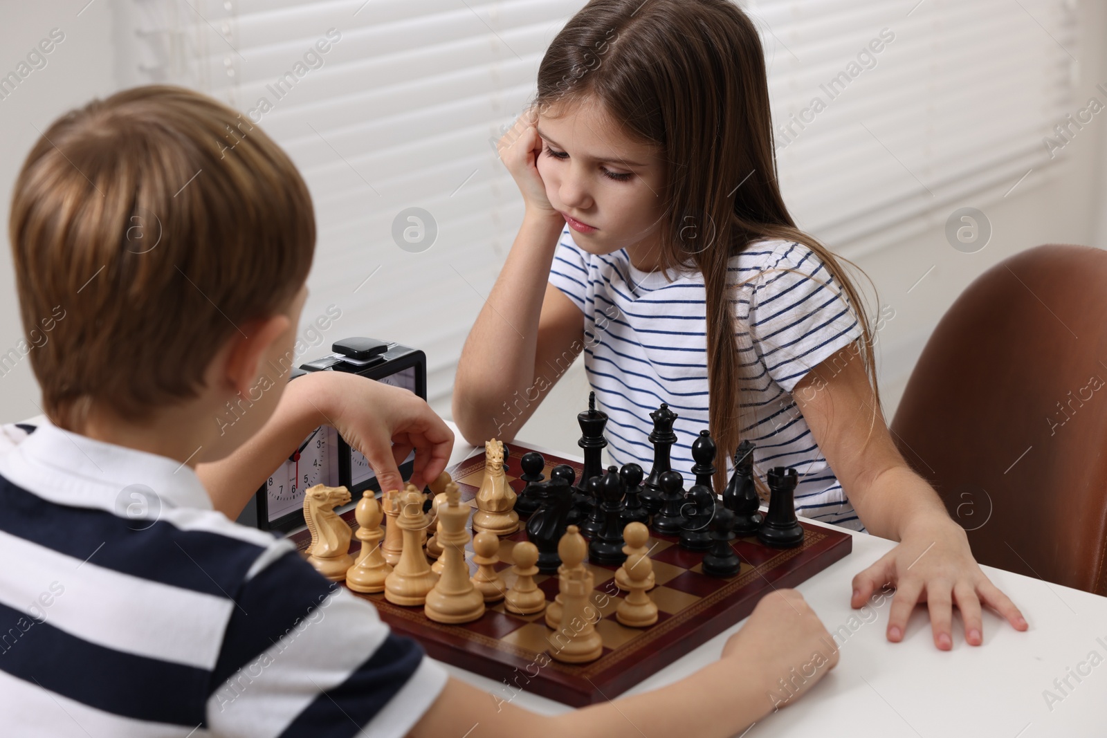 Photo of Cute children playing chess at table in room