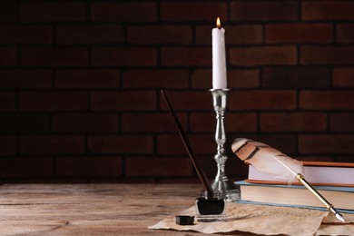 Photo of Inkwell, feather pen, candlestick and vintage parchment on wooden table indoors. Space for text