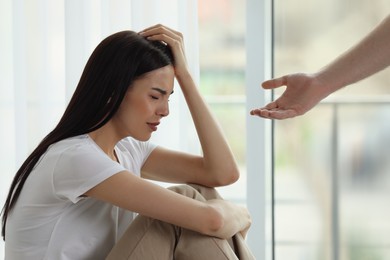 Photo of Man offering hand to depressed woman indoors