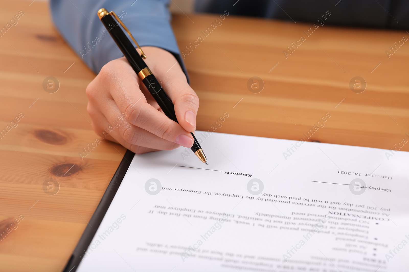 Photo of Businesswoman signing contract at wooden table, closeup of hands