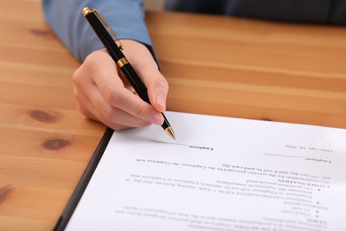 Businesswoman signing contract at wooden table, closeup of hands