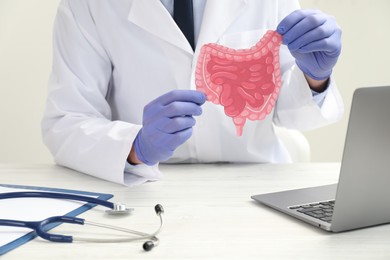 Photo of Doctor with paper intestine cutout at white wooden table, closeup