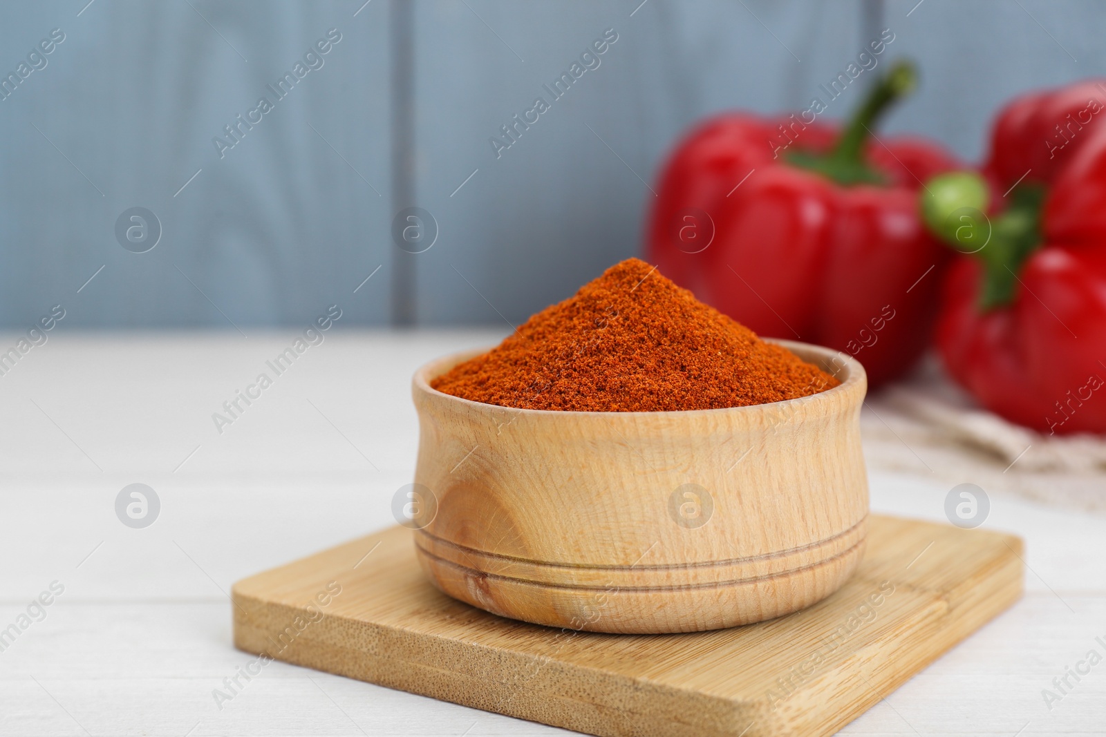 Photo of Bowl with aromatic paprika powder and fresh bell peppers on white table