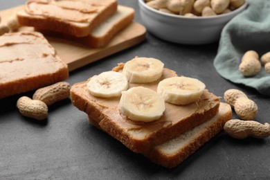 Photo of Tasty peanut butter sandwiches with sliced banana and peanuts on dark gray table, closeup