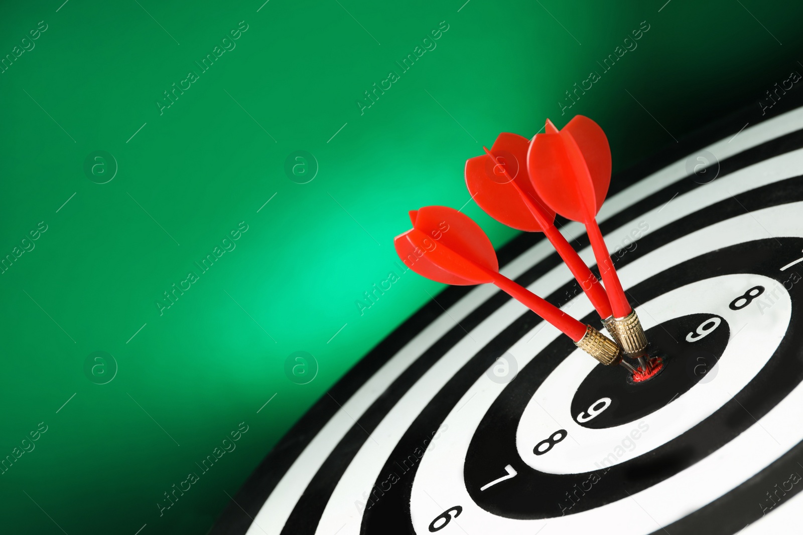 Photo of Red arrows hitting target on dart board against green background. Space for text