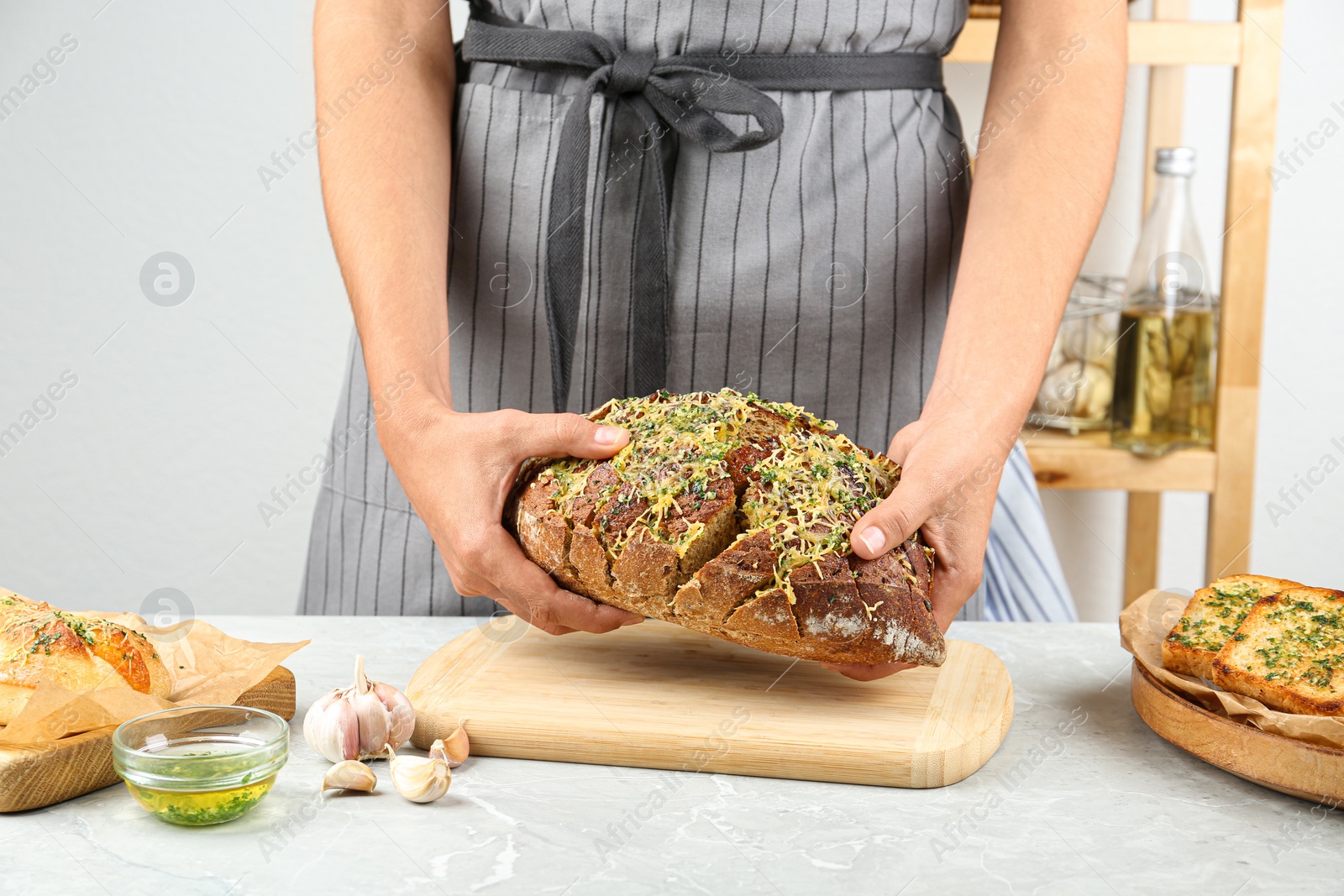 Photo of Woman breaking tasty homemade garlic bread with cheese and herbs at grey table, closeup