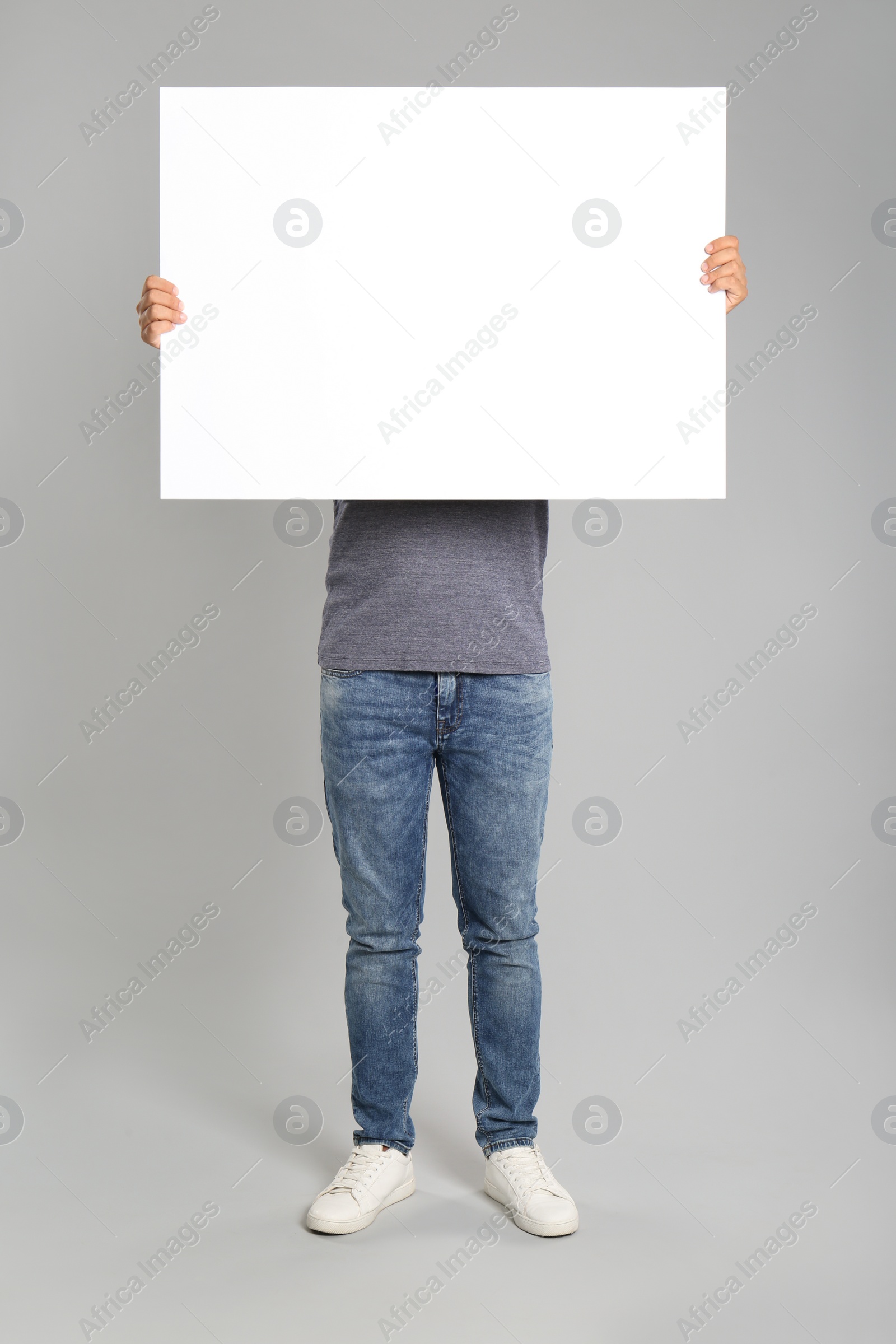Photo of Man holding white blank poster on grey background. Mockup for design