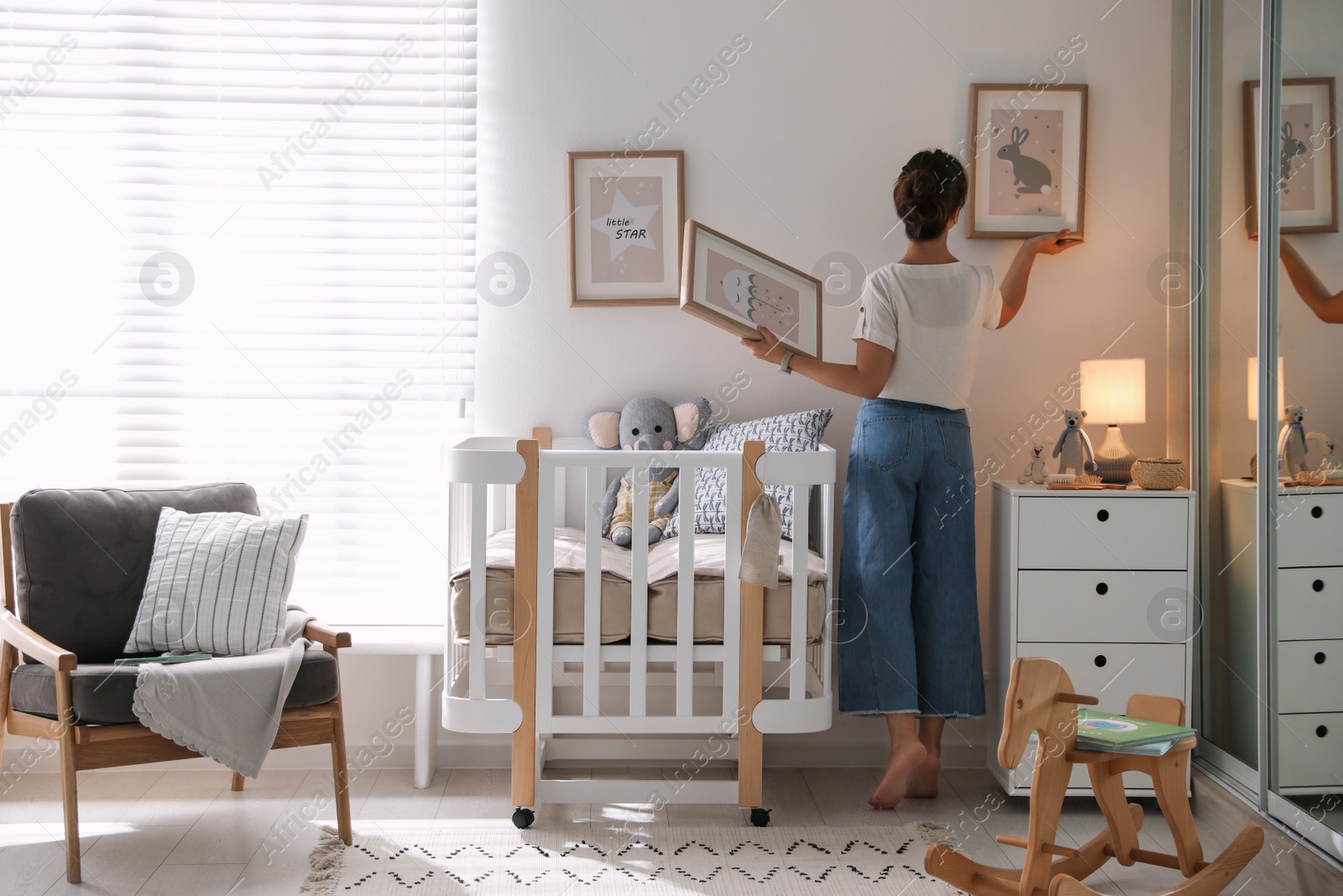 Photo of Decorator hanging pictures on wall in baby room. Interior design