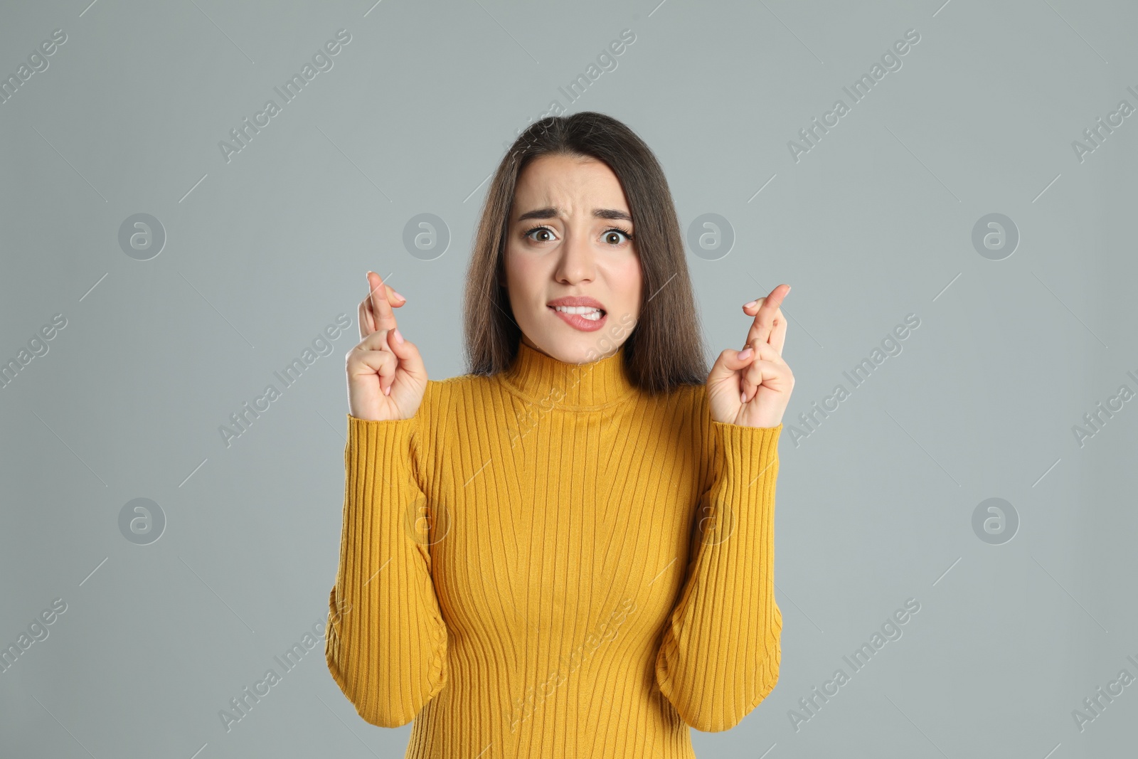 Photo of Nervous young woman holding fingers crossed on grey background. Superstition for good luck