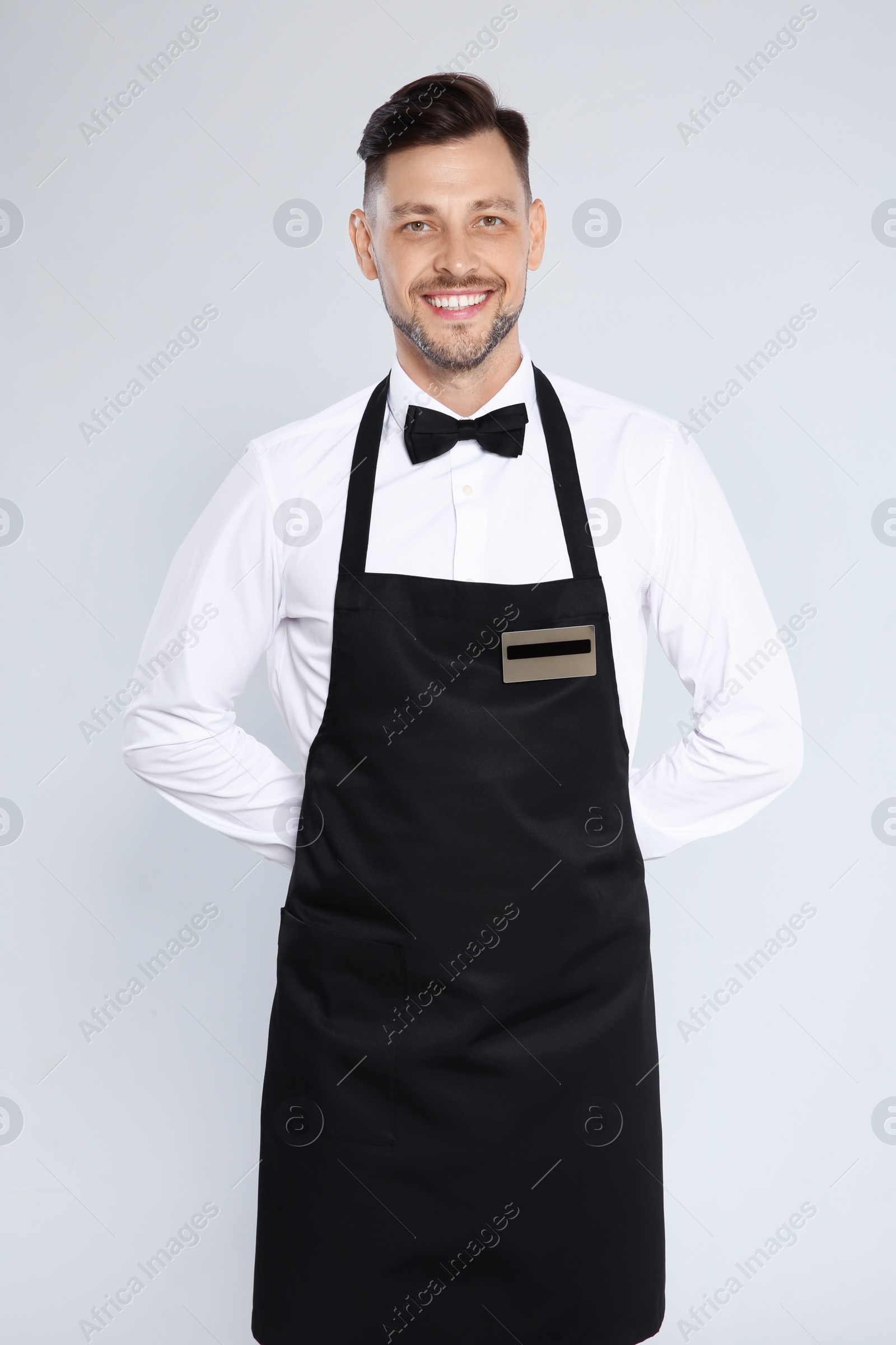 Photo of Portrait of handsome waiter in elegant uniform on light background