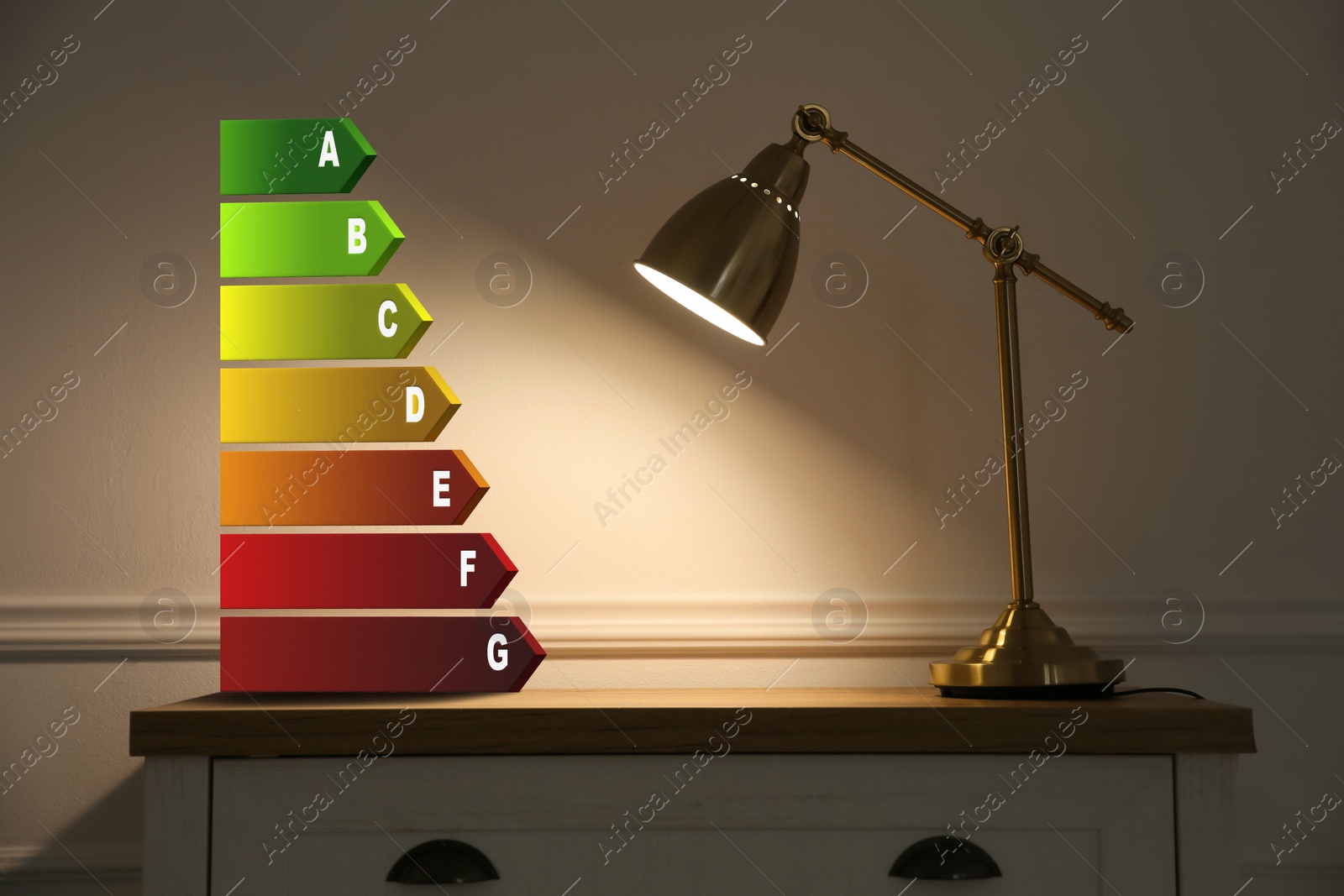 Image of Energy efficiency rating label and lamp on wooden chest of drawers near beige wall indoors