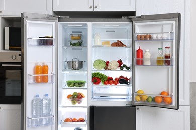 Open refrigerator full of different products in kitchen