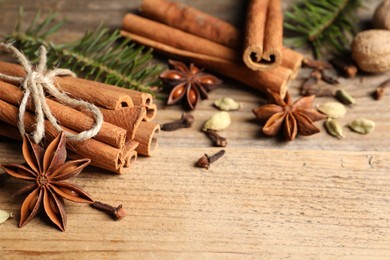 Different aromatic spices and fir branches on wooden table, closeup. Space for text