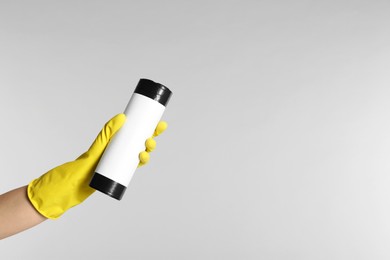 Janitor in rubber glove holding roll of black garbage bags on light grey background, closeup. Space for text