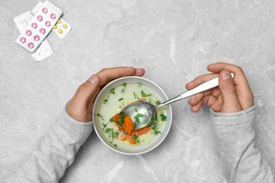 Photo of Man with bowl of soup at grey marble table, top view. Flu treatment