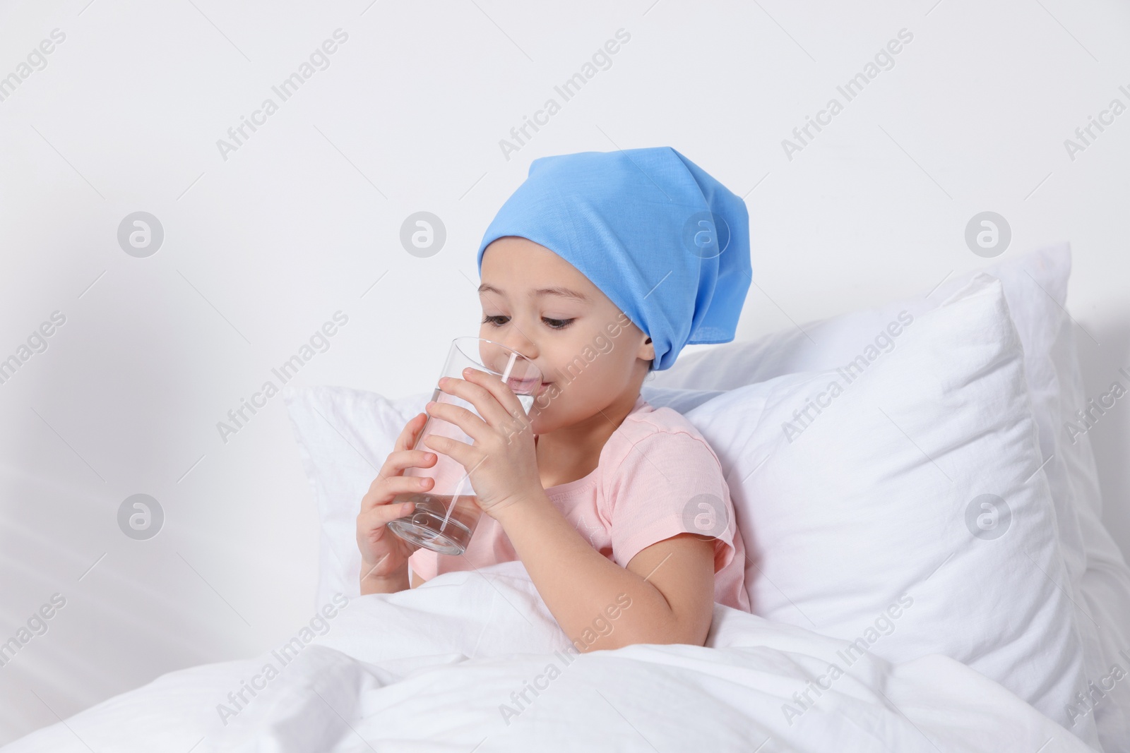 Photo of Childhood cancer. Girl drinking glass of water in bed indoors