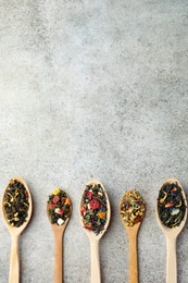 Photo of Different kinds of dry herbal tea in wooden spoons on light grey table, flat lay. Space for text