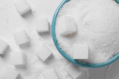 Different types of sugar in bowl on white table, flat lay