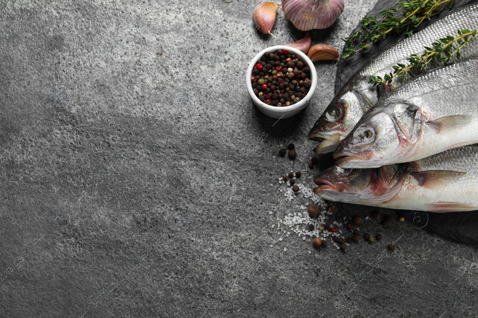 Photo of Tasty sea bass fish on grey textured table, flat lay. Space for text