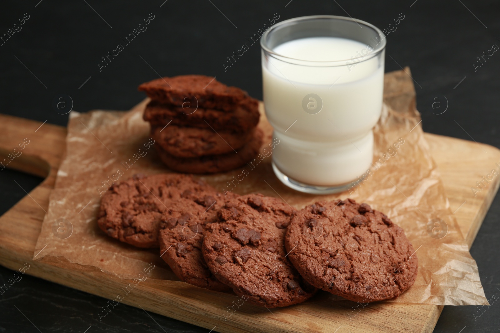 Photo of Board with tasty chocolate cookies and glass of milk on table, closeup