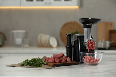 Photo of Electric meat grinder with beef mince and parsley on white table in kitchen
