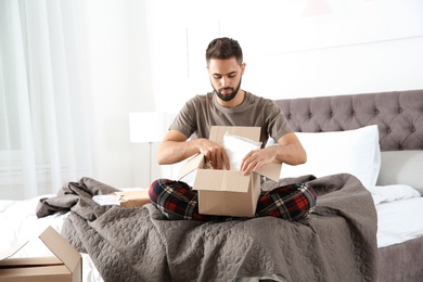 Photo of Young man opening parcel in bedroom at home