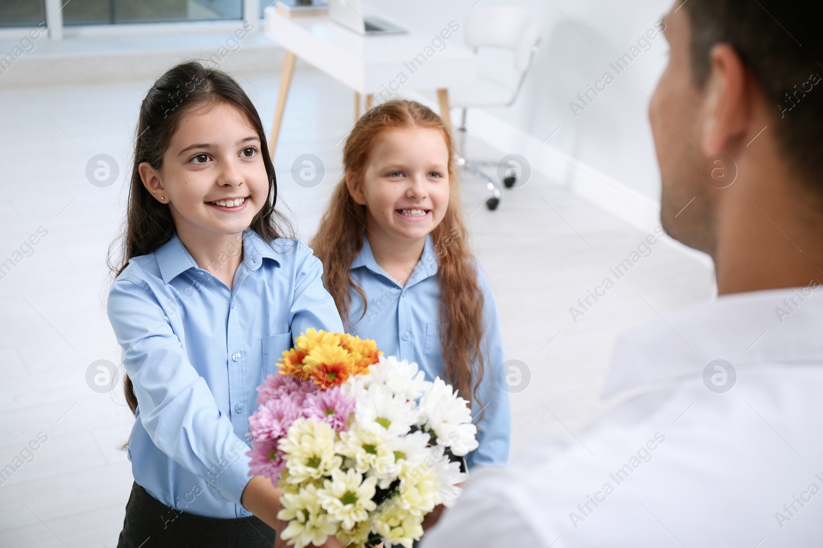 Photo of Schoolgirls congratulating their pedagogue with bouquet in classroom. Teacher's day